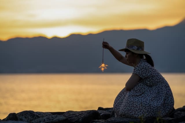 夏の夕暮れ、砂浜で線香花火に興じる人物の画像
