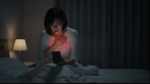 夜中に胸やけで苦しみ、スマートフォンで逆流性食道炎について検索する女性。