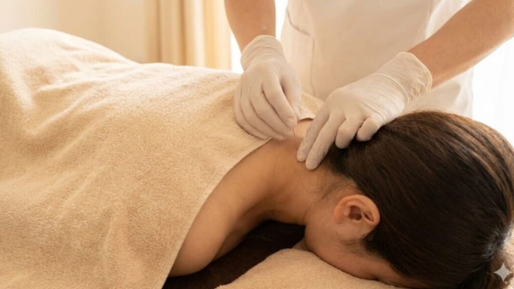 浜崎鍼灸整骨院で、白衣を着た50代の男性鍼灸師が、うつ伏せになった女性患者の首筋に慎重に鍼を打っている治療風景。