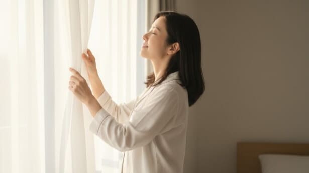 朝日を浴びる日本人女性がカーテンを開けて窓際に立っている爽やかな朝の風景